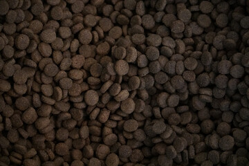 Full frame close-up texture of dark brown dry pet food kibble pellets for background use in animal nutrition and retail themes © Michael