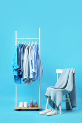 Different clothes hanging on rack, shoes, blanket and chair against light blue background