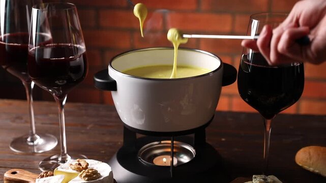 Women dipping pieces of different snacks into fondue pot (caquelon) with melted cheese at wooden table indoors, closeup