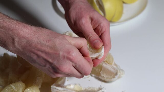 A close up demonstration meticulously peeling a fresh, juicy pomelo segment using a small orange tool, for a healthy fruit snack on a white surface
