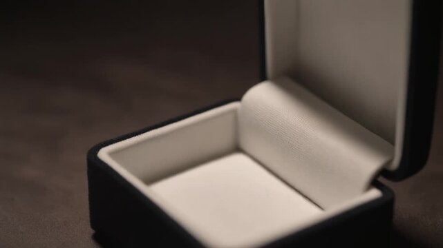 Luxury black jewelry box with white velvet interior open on a dark background.