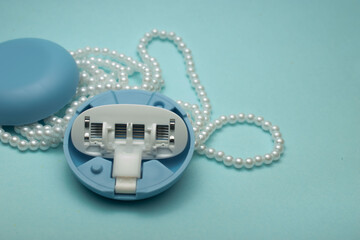 Minimal still life featuring a modern razor styled with pearls and soft blue elements on a pastel...