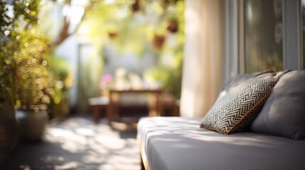 Fototapeta premium Sunlit outdoor seating area with a comfortable gray sofa featuring decorative pillows, soft curtains, and blurred greenery in the background