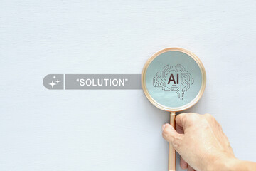 Hand holding magnifying glass focusing on AI brain icon and Solution text on white backdrop. Concept of using future artificial intelligence technology to find smart answers for business innovation.