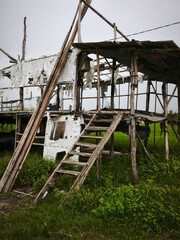 a Long Dilapidated Bamboo Structure with Torn White Tarpaulin Covers on a Rural Farm, Featuring a Rustic and Abandoned Architectural Style in a Grassy Field