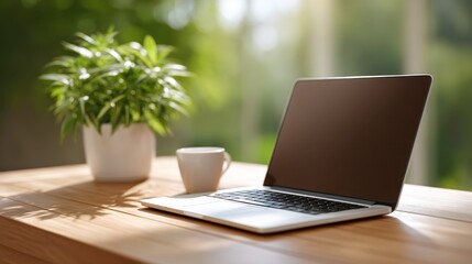 Fototapeta premium Modern workspace with laptop, coffee cup, and potted plant on wooden table in bright, natural light creating an inviting atmosphere for productivity
