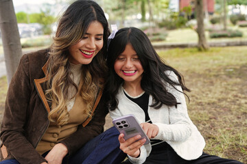 Mother and daughter using smartphone outdoors sharing happy moments