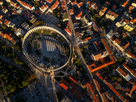 Pula Arena ancient Roman amphitheater with historic city skyline and orange roofs aerial drone view.
