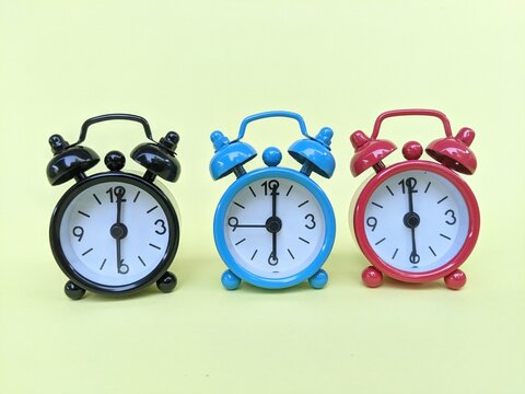 Three colorful analog alarm clocks set to 6:00, showcasing classic design and synchronized time against a pastel background