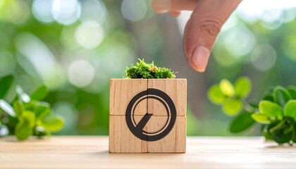 A hand touches a wooden block with a clock symbol and green growth on top