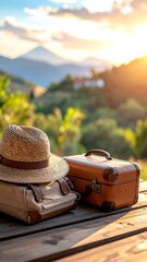 Luggage & straw hat sit on wooden table, mountain view, sunlit foliage background