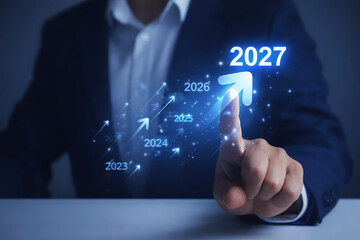 Forecast Businessman hand pointing at glowing rising arrow and 2027 year text for financial growth forecast and economic progress success strategy concept on blue background