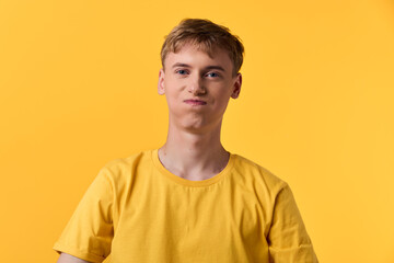Young man in a yellow t shirt on a solid yellow backdrop, casual pose, minimal studio shot...