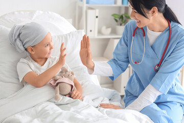 Little girl after chemotherapy giving high-five to nurse in clinic. Childhood cancer awareness...