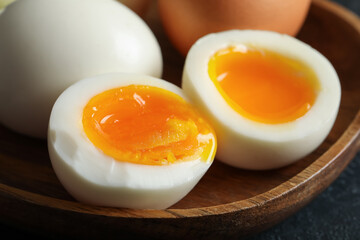 Wooden plate with soft boiled eggs on dark background, closeup