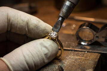 Jeweler setting a diamond into a gold ring using a pushing tool