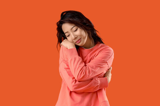 Young Asian woman hugging himself on orange background