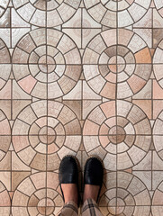 personal perspective woman wearing black casual shoes standing on brown colour pattern tiled floor