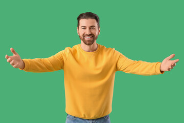 Young man opening arms for hug on green background