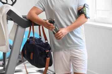 Man with bottle of water and sports bag on treadmill at gym