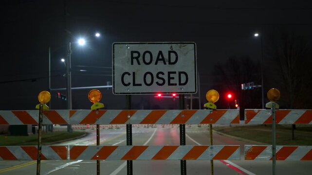 Road closed sign with illuminated construction barriers at night. traffic control, road maintenance, public safety infrastructure, nighttime construction work. POV view