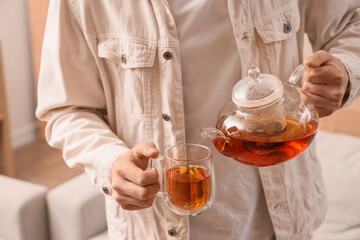 Young man pouring tea into glass cup at home, closeup