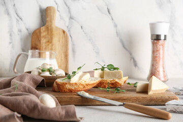 Wooden board with fresh bread, triangles of tasty processed cheese, micro green and mushrooms on...