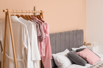 Comfortable bed and rack with clothes in interior of bedroom