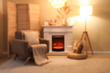 Naklejka premium Blurred view of cozy living room with fireplace, armchair and glowing lamps
