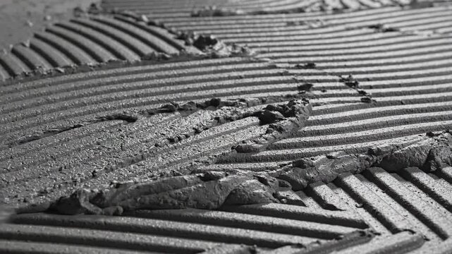 Close up of a trowel spreading thinset mortar onto a surface creating ribbed patterns for tile installation construction work detail shot overhead view with dramatic lighting