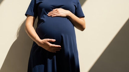Expecting mother in blue dress gently cradling baby bump against sunlit wall. Expecting mother portrays joy and anticipation of pregnancy while showcasing her beautiful curves in stylish dress.