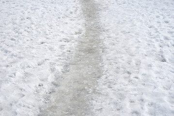 Frozen path in the city park in winter. Melting snow with footprints on the left and right side of the path.