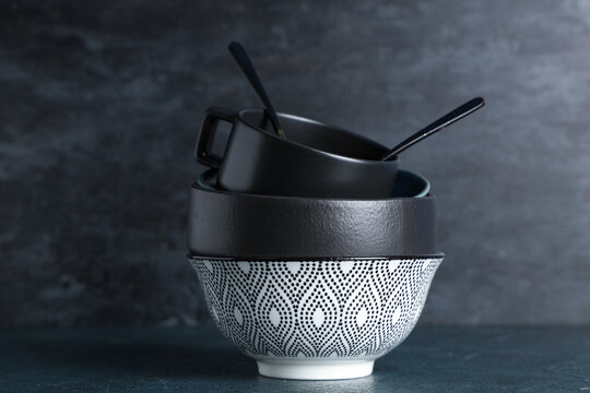 Stack of clean tableware and cutlery on table against black grunge background - Powered by Adobe