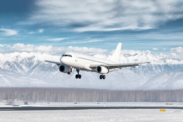 White passenger plane landing at winter airport on the background of high snow capped mountains