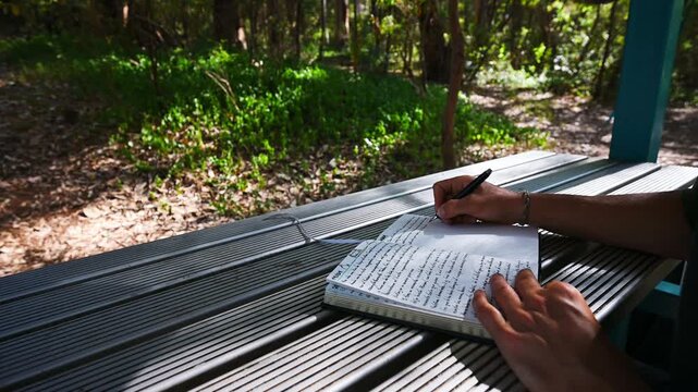 Person writing in notebook at outdoor table in forest setting