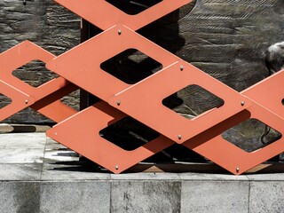 A close-up of vibrant orange metal geometric panels with a diamond lattice design. This architectural detail showcases modern industrial art and bold structural patterns outdoors.