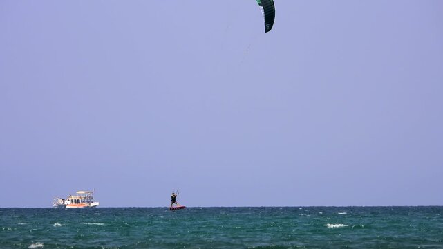 Kiteboarding and kitesurfing as a kiter is pulled across sea water by a power kite. Kiteboarders and kitesurfers ride wind power near the beach for extreme sea sport.