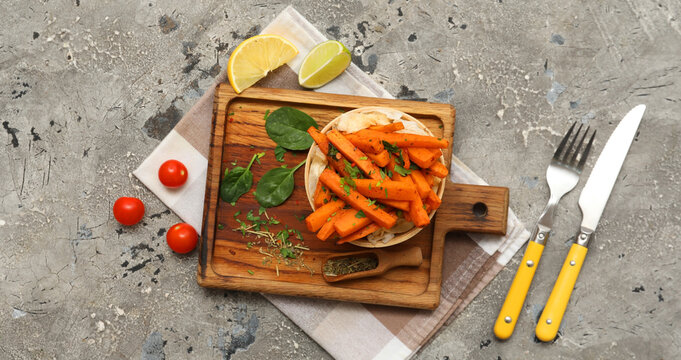 Bowl with baked sweet potato, tomatoes, spinach leaves and cutlery on grey grunge background