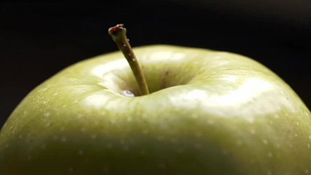Closeup of a green apple with a stem on a dark background