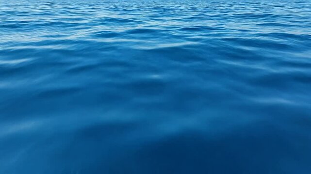 Deep sapphire blue ocean waves moving gently under soft daylight, filmed from a low angle skimming the surface, creating an abstract liquid texture and serene mood.