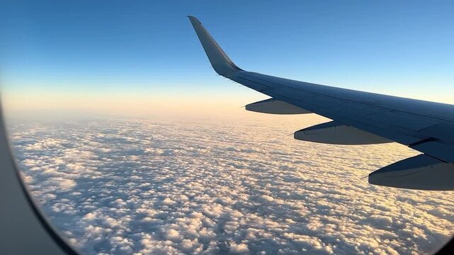 View from plane window wing over endless sunlit clouds, blue sky meets golden horizon