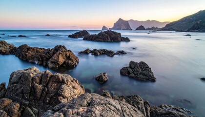 Serene rocky coastline at dusk with calm waters and distant mountains.