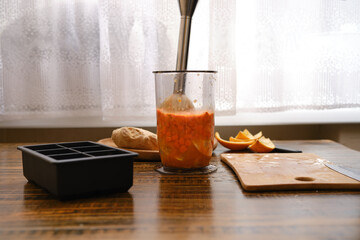 Mixing sea buckthorn and orange in a jar with immersion blender on a wooden table near the window