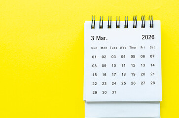 Top view of March 2026 table calendar with space for text on yellow background.