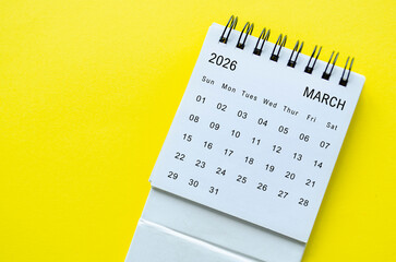 White spiral desk calendar for March 2026 on yellow background with simple visual balance and space for text.