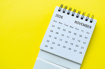 White spiral desk calendar for November 2026 on yellow background with clean framing and space for text.