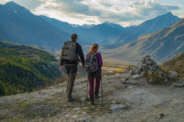 Rear view of two hikers, a man and a woman, standing on a mountain ridge overlooking a stunning...