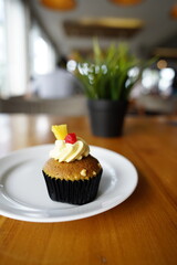 a cupcake on a white plate on a wooden table, breakfast menu in the morning, with natural lighting in the morning