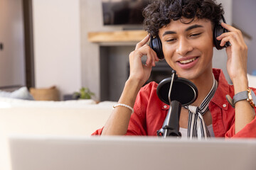 Man adjusting over-ear headphones while leaning toward microphone at desk in living room