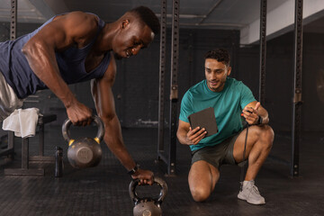 Diverse coach and client training with kettlebells in gym weight area using tablet and stopwatch
